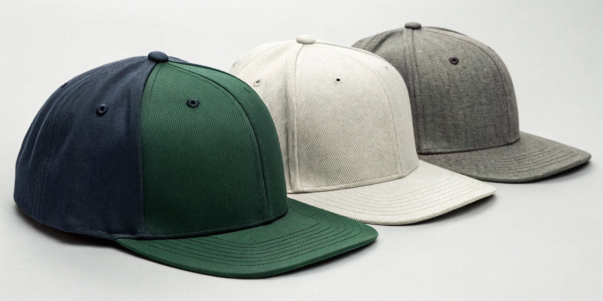 Béisbol Dandy snapback hats in green, cream, and gray on display.